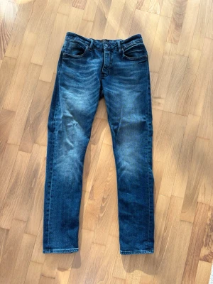 Neuw jeans lou slim - Snygga mörkblå jeans från NEUW med slim fit passform och klassisk femficksdesign. Jeansen har en lätt tvättad look med slitningar på låren och raka ben. Perfekta för en avslappnad och trendig stil.