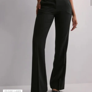 Svarta vida kostymbyxor - Säljer ett par svarta kostymbyxor med låg midja och vida ben. Byxorna har en klassisk pressveck framtill och är tillverkade i ett mjukt, vävt material som ger en snygg siluett. Perfekta för dig som gillar stilrena och trendiga plagg.