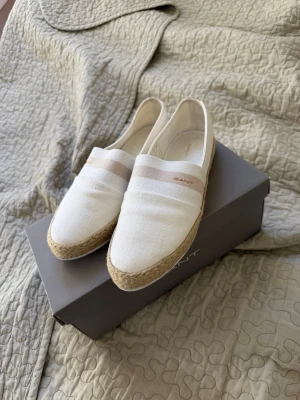 Vita espadrillos från Gant - Snygga vita espadrillos från Gant i linnematerial med naturfärgad flätad sula. Skorna har en diskret beige rand och Gant-logga på sidan. Storlek 38, knappt använda.