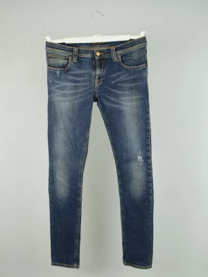 Nudie Jeans  - NUDIE JEANS Storlek : W30/L34 Modell : Tight Long Jon Mått : A = 40CM - B = 105CM Användning : Jeansen är i ett fint skick utan defekter Nypris : Cirka 2000SEK Modellen på bilden : 182CM och väger 78KG