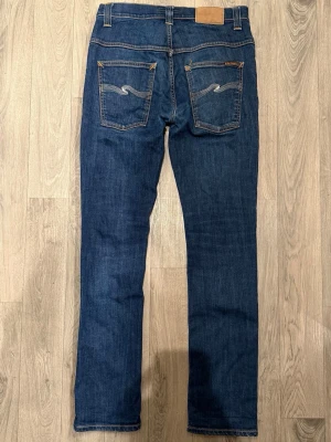 Nudie Jeans Thin Finn Organic Dry Mörkblå W31 L32 - Sjukt snygga mörkblåa Nudie Jeans Thin Finn ’Dry Ecru Embo” i fint skick (Endast liten slitning i skrevet och litet hål i ena fickan). Mått - Midja: 39cm, Benlängd: 102cm. Modellen är 185cm & 63kg. Hör av dig vid funderingar!🤝