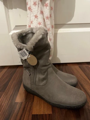 Gråa fodrade stövlar med dragkedja - Säljer ett par gråa stövlar i mockaimitation med mjukt, fluffigt foder och dragkedja på sidan. Skorna har en låg sula och enkel design som passar till många outfits. 