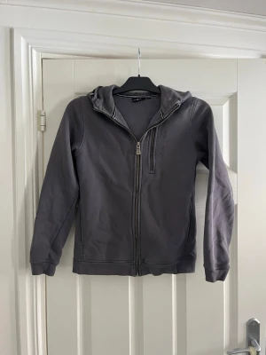 Mörkgrå hoodie med dragkedja - En mörkgrå hoodie med dragkedja framtill och huva. Storlek 160.
