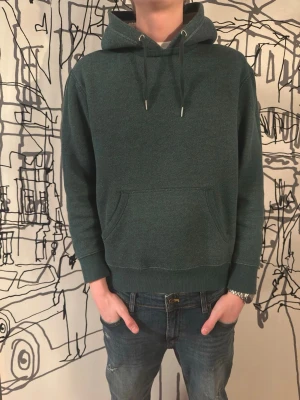 Fodrad hoodie - En väldigt sällsynt och eftertraktad Mysig mörkgrön hoodie med huva och dragsnören. Insidan av huvan är fodrad med vitt teddyfoder för extra värme. Klassisk känguruficka framtill och ribbade muddar vid ärmar och nederkant. Perfekt för dig som gillar en avslappnad och bekväm stil.