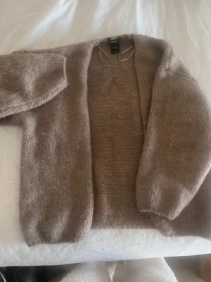 Beige stickad kofta från Lindex - Mysig beige stickad kofta från Lindex med öppen front och ballongärmar. Koftan är gjord i ett mjukt material och har en avslappnad passform som passar perfekt till lager på lager. Enkel att matcha med olika outfits.