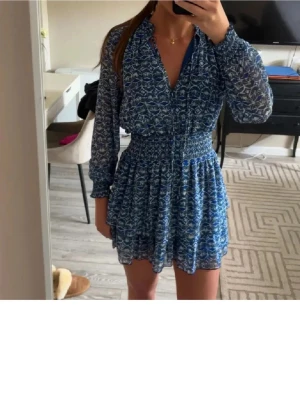 Blå kort klänning med mönster - Supersöt blå kort klänning med vitt mönster och långa transparenta ärmar. Mycket bra skick och sparsamt använd!!