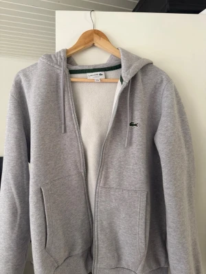 Grå zip-hoodie från Lacoste - Snygg grå zip-hoodie från Lacoste med klassisk passform. Tröjan är i nyskick den är i storlek m och passar även S, pris kan diskuteras vid snabb affär 