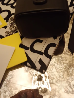 Svart boxformad handväska från Marc jacobs - Snygg svart boxformad handväska från Marc jacobs med silverfärgad kedjerem och dragkedja runt locket. Väskan har en stilren design och är tillverkad i slätt konstläder. Perfekt accessoar för dig som gillar trendiga detaljer och logotypmönster.