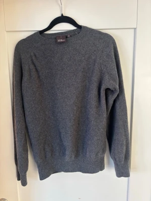Grå stickad tröja Oscar Jacobson - Klassisk grå stickad tröja från Oscar Jacobson. Tröjan har rund halsringning, långa ärmar och ribbade muddar vid ärmslut och nederkant. Tillverkad i Italien och perfekt för lager på lager under kyliga dagar.