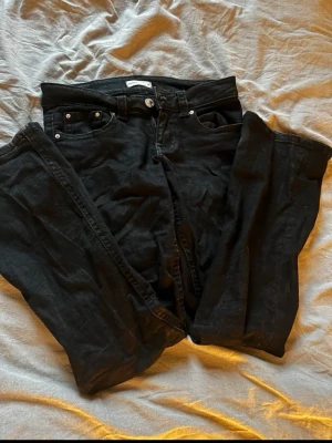 Svarta jeans med knappfickor bak - Säljer ett par svarta jeans. Jeansen har silverfärgade knappar på bakfickorna och normal midja. Materialet är denim i bomull. Perfekta till en avslappnad look.