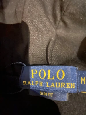 Svart hoodie från Polo Ralph Lauren - Snygg svart hoodie från Polo Ralph Lauren i slim fit-modell. Hoodien har klassisk huva och ribbade muddar vid ärmslut och nederkant. Tillverkad i mjukt material som känns skönt mot huden. Perfekt för dig som gillar stilrena och tidlösa plagg.