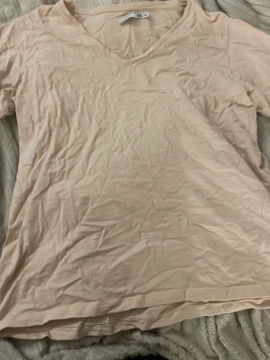 Beige v-ringad t-shirt från 157 - Ljusbeige t-shirt från 157 med v-ringning och korta ärmar. Tillverkad i mjuk bomull som känns skön mot huden. Enkel och clean design som passar till det mesta. Den är mer åt det rosa hållert än vad som syns i bild💕