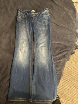 Blå bootcut jeans med slitningar - Säljer ett par blå bootcut jeans med snygga slitningar och ljusare partier framtill. Jeansen har klassisk femficksdesign, normal midja och vida ben. Perfekta för dig som gillar retrostil och vill ha ett par jeans som sticker ut. Ganska mörka i färgen. Storlek M och långa i benen! 💕 