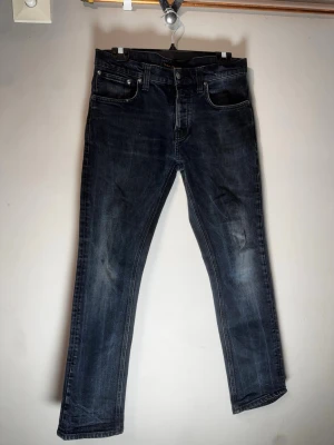 Mörkblå jeans från Nudie Jeans - Snygga mörkblå jeans från Nudie Jeans med klassisk femficksmodell och raka ben och kontrastsömmar samt Nudie-logga på bakfickan. Tillverkade i denim med en cool tvättad look.