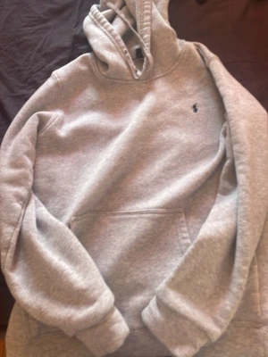Grå hoodie från Polo Ralph Lauren - Snygg grå hoodie från Polo Ralph Lauren med klassisk huva och dragsko. Tröjan har en känguruficka framtill och den ikoniska lilla broderade loggan på bröstet. Tillverkad i mjukt bomullsmaterial som är perfekt för chill dagar.pris kan diskuteras