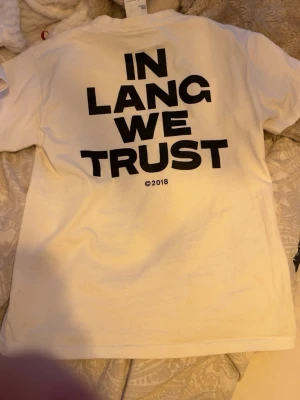 Vit Helmut Lang t-shirt med tryck - Kan gå ner i pris 🙏Vit t-shirt från Helmut Lang med svart texttryck 'IN LANG WE TRUST' på ryggen och liten logga fram. Klassisk rund hals och korta ärmar. Tillverkad i mjuk bomull för en skön känsla och enkel stil.