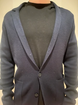 Mörkblå stickad kavaj med två knappar - Mörkblå kavaj i stickat material med två knappar framtill och två framfickor. Klassisk krage och mjuk, avslappnad passform som ger en modern look. Perfekt för dig som vill ha en stilren men bekväm kavaj. Mitt pris 749kr. Jag är 186 cm lång o väger 75kg!