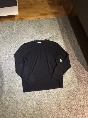 Svart merinoullströja These Glory Days - Klassisk svart stickad tröja från These Glory Days i mjuk superior merinoull. Tröjan har rund halsringning och långa ärmar, perfekt för lager på lager och stilrena outfits.