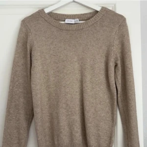 Beige stickad tröja från Vila - Mysig beige stickad tröja från Vila med rund halsringning och ribbade muddar vid ärmslut och nederkant. Perfekt basplagg i garderoben som är lätt att matcha till olika outfits.