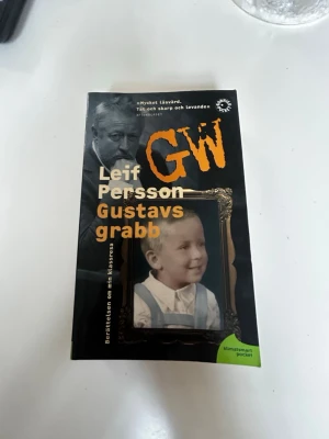 Gustavs grabb av Leif GW Persson - En svart pocketbok med titeln 'Gustavs grabb' av Leif GW Persson. Omslaget har en gul text och ett foto i ram av ett barn. Boken är en självbiografisk roman och utgiven av Bonnier Pocket. Klimatsmart pocket-etikett syns på framsidan.