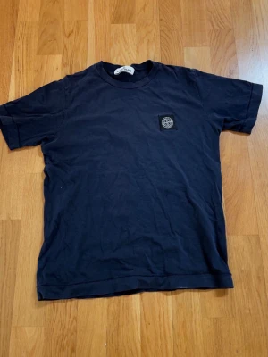 Mörkblå Stone Island t-shirt - Snygg mörkblå t-shirt från Stone Island med klassisk rund hals och ikonisk patch med logga på bröstet. Tillverkad i mjuk bomull som känns skön mot huden. Perfekt för dig som gillar streetwear och vill ha en enkel men stilren look.