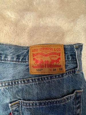 Levi's 555 blå raka jeans - Klassiska blå Levi's 555 jeans med straight/relaxed passform. Tillverkade i slitstark denim med den ikoniska läderlappen bak i midjan. Perfekta för dig som gillar tidlös och avslappnad stil. Passar till allt och knappt använd. Angiven storlek är W34 L32, men waisten upplevs snarare som W33/32 
