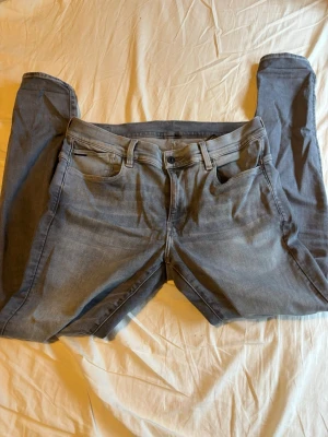 Ljusgrå jeans från G-Star - Snygga ljusblå jeans från G-Star med klassisk femficksmodell och raka ben. Jeansen har en diskret logga vid myntfickan och är gjorda i mjukt denimtyg som sitter skönt. Perfekta för dig som gillar stilrena och tidlösa jeans. Jeansen är slim fit 