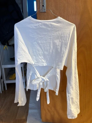 Vit långärmad topp med knyt - Vit långärmad topp med snygg knytning i ryggen. Har en croppad passform