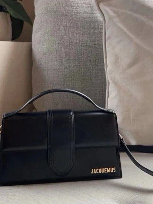 Svart läderväska  - Säljer en svart handväska i slätt faux skinn med guldfärgad logga. Väskan har ett stilrent, rektangulärt format och både handtag och axelrem för olika sätt att bära. Dustbag ingår (ej prislapp!!)☀️