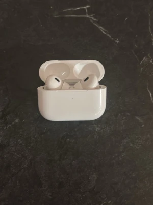 AirPods Pro (2:a generationen) - Säljer ett par vita Apple AirPods Pro med trådlöst laddningsetui. Hörlurarna har silikonproppar för extra komfort och brusreducering. Medföljer laddningskabel ochi extra öronproppar i olika storlekar. Snygg och stilren design i plast.