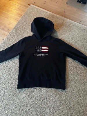 Mörkblå Lexington hoodie med tryck - Snygg mörkblå hoodie från Lexington med broderat amerikanskt flaggtryck och texten 'American Heritage Since 1993' på bröstet. 