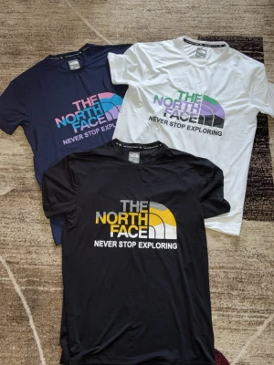 The North Face t-shirts i tre färger - Använt max 2 gånger. Säljer tre snygga t-shirts från The North Face i svart, vit och marinblå. Alla har korta ärmar och stort tryck framtill med logga och texten 'Never Stop Exploring'. Materialet känns mjukt och sportigt, perfekt till vardags. Klassisk passform och rund hals.