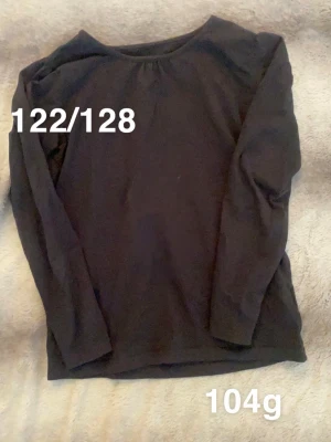 Svart långärmad topp - En enkel svart långärmad topp med rund halsringning. Perfekt basplagg att matcha med olika stilar. 🌸 Fint använt skick. Storlek 122/128