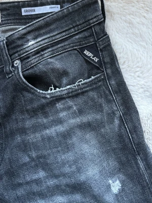 Replay svarta straight fit jeans - Säljer ett par svarta Replay jeans i modellen Grover med straight fit. Jeansen har slitna detaljer, råa kanter vid fickan och lätt tvättad look. Klassisk femficksmodell med dragkedja och knapp. Perfekta för en avslappnad och trendig stil.