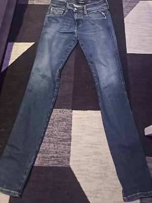 Mörkblå slim fit jeans från replay  - Snygga mörkblå slim fit jeans från replay med klassisk femficksdesign och diskreta slitningar. Jeansen har raka ben och normal midja, perfekta för en trendig och avslappnad look. Materialet är mjukt och stretchigt för extra komfort.