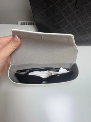 Svarta solglasögon från Michael Kors - Snygga svarta solglasögon från Michael Kors med rektangulär form och guldfärgade MK-detaljer på sidorna. Glasögonen kommer med ett vitt fodral och putsduk. Perfekt för dig som vill ha en stilren och trendig look.