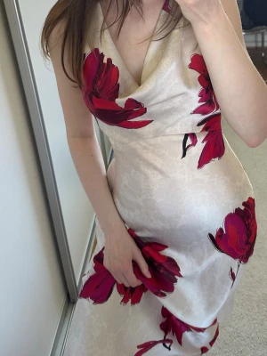 Blommig halterneckklänning i satin - Halterneckklänning i  satin med stora röda blommor och öppen rygg. Klänningen har en v-ringad front och ett  spänne i nacken. Från Zara, använd få gånger🩷