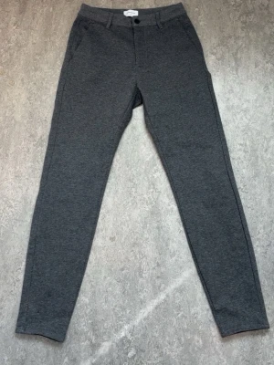 Grå mjukisbyxor från Studio Total - Snygga grå mjukisbyxor från Studio Total med slim fit och klassisk knappstängning. Byxorna har fickor på sidorna och är gjorda i ett mjukt och bekvämt material som passar perfekt för chill dagar. Enkel och stilren design som är lätt att matcha.