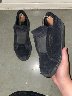 Svarta slip-on sneakers från Axel Arigato - Säljer ett par svarta slip-on sneakers från Axel Arigato i mocka. Skorna är i okej skick . Små hål i båda skorna . Märket är kvar på båda skorna . Ändå användbara och passar till de mesta riktigt stilrena.