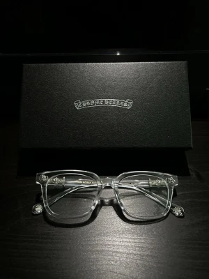 Chrome Hearts solglasögonfodral - Snyggt svart solglasögonfodral från Chrome Hearts med logga i silver på locket. Perfekt för att förvara och skydda dina solglasögon med stil. Fodralet har en lyxig känsla och passar dig som gillar exklusiva accessoarer.