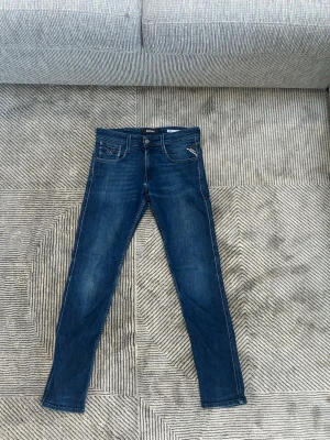 Replay ambass jeans  - Snygga blå slim fit jeans från Replay, modell Anbass. Jeansen har klassisk femficksdesign, dragkedja och knappstängning samt diskreta slitningar. Perfekt passform och cool look för dig som gillar stilrena jeans.