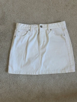 Vit kort jeanskjol med fickor - Säljer en vit jeanskjol med klassiska fickor fram och bak samt knapp och dragkedja i midjan. 