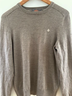 Grå stickad tröja från Morris - Klassisk grå stickad tröja från Morris med rund halsringning och diskret logga broderad på bröstet. Tröjan har långa ärmar och ribbade muddar vid ärmslut och nederkant. Perfekt basplagg i mjukt material. Passar dig perfekt mellan 165-175