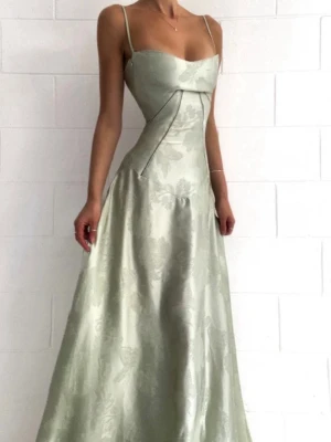 Ljusgrön långklänning med snörning - Elegant ljusgrön långklänning med tunna axelband och subtilt blommönster. Klänningen har figurnära överdel, utsvängd kjol och snygg snörning i ryggen för perfekt passform. Tillverkad i glansigt material som ger en lyxig känsla.