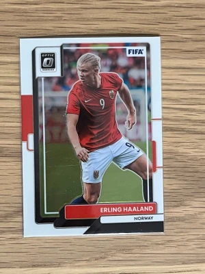 FIFA Panini fotbollskort Haaland - Säljer ett FIFA Panini fotbollskort med Erling Haaland från Norge. Kortet har en färgstark design med Erling Haaland i röd matchtröja och vita shorts. Optic Donruss-serien, nummer 84. Perfekt för samlare av fotbollskort och fans av internationell fotboll.