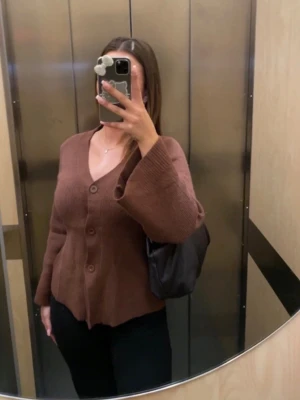 Brun stickad kofta med knappar - Mysig brun stickad kofta med tre knappar framtill och v-ringad hals. Koftan har långa ärmar och en något lös passform, perfekt för lager-på-lager. Materialet ser ut att vara mjukt och bekvämt, perfekt för kyligare dagar.Sjukt bekväm och snygg stickad tröja med knappar i färgen brun. Tröjan har vida armar. Helt ny och oanvänd, storlek S men upplevs lite större i storleken, super gosig och skön. Passar perfekt för våren då den inte är jätte tjock i materialet.