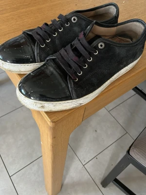 Lanvin skor - Svarta sneakers med snygg lackad tå och svarta skosnören. Ovandelen är i mockaliknande material och sulan är vit med slitna detaljer. Perfekta för dig som gillar en stilren men ändå edgy look.