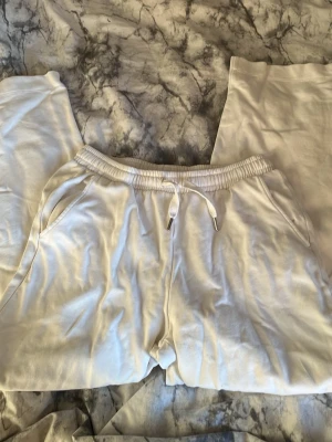 Vita mjukisbyxor - Säljer ett par vita mjukisbyxor. Byxorna har två sidofickor och är gjorda i ett mjukt och bekvämt material, perfekt för chill dagar. Passformen är relaxed och tyget är bomullsmix.