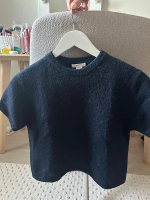 Mörkblå stickad kortärmad topp - En enkel och stilren mörkblå stickad topp med korta ärmar och rund hals. Perfekt att matcha med jeans eller kjol för en avslappnad look. Mjuk och skön mot huden.