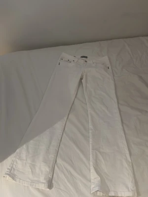 Vita bootcut jeans - Snygga vita bootcut jeans med klassisk femficksdesign och låg midja. Jeansen har raka ben och är tillverkade i ett stretchigt bomullsmaterial för en bekväm passform. Perfekta för dig som vill ha en fräsch och stilren look.